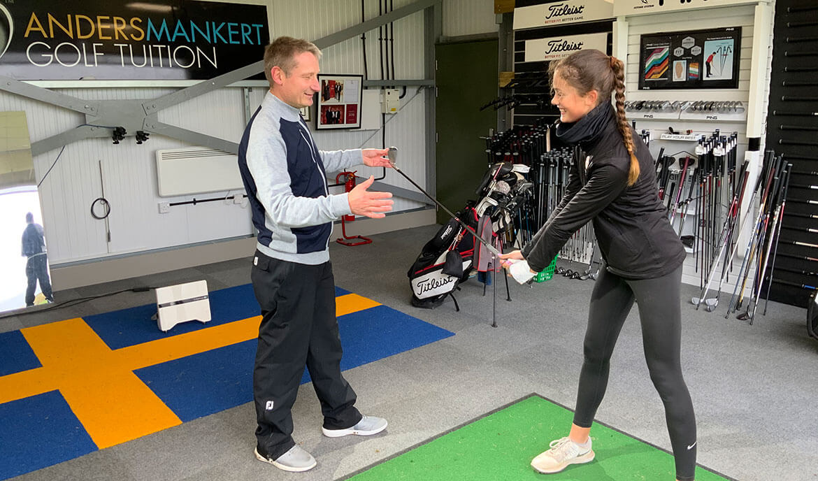 Young woman swinging club with Anders instructing